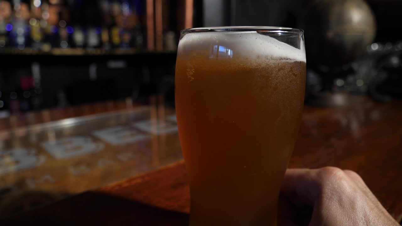 Mano posa un bicchiere di birra su un bancone di legno