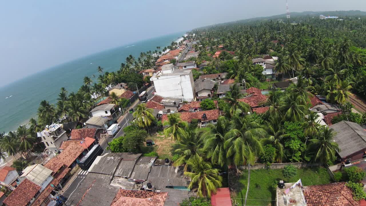 fpv volando sobre una zona residencial cubierta de palmeras verdes cerca del océano azul, sri lanka