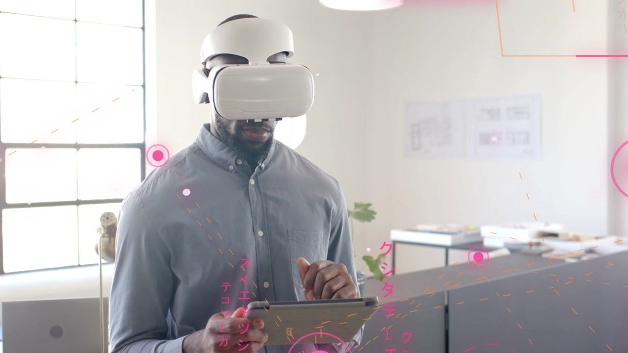 Uomo afroamericano che indossa una camicia grigia, tiene un tablet e usa un visore VR bianco vicino alla finestra dell'ufficio