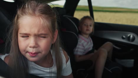 Niña-Caucásica-De-8-Años-Mirando-Por-La-Ventana-Del-Auto-Mientras-Viaja-En-Auto-Y-Su-Hermana-Al-Fondo.