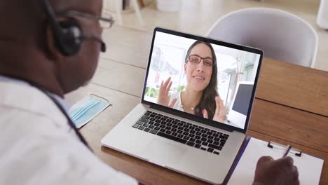 hombre de negocios afroamericano sentado en un escritorio usando una computadora portátil haciendo una videollamada con una colega