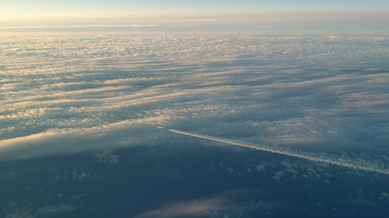 Incredible view from the cockpit of an airplane flying high above the clouds leaving a long white condensation vapour air trail in the blue sky