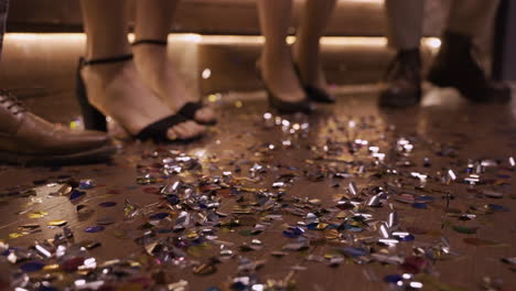 camera focuses on the wooden floor full of confetti and men shoes and women heels moving while they dance 1