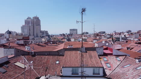 Disparo-De-Un-Dron-De-Pedestal-Que-Se-Eleva-Por-Encima-De-Un-Techo-Tradicional-Español-De-Tejas-De-Barril-Para-Revelar-El-Mayor-Paisaje-Urbano-Del-Barrio-De-Malasaña-En-Madrid,-España