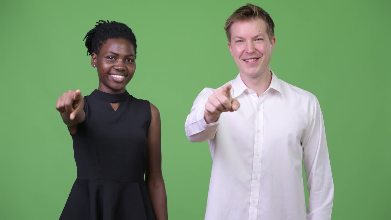 Two young multi-ethnic business couple pointing at camera together
