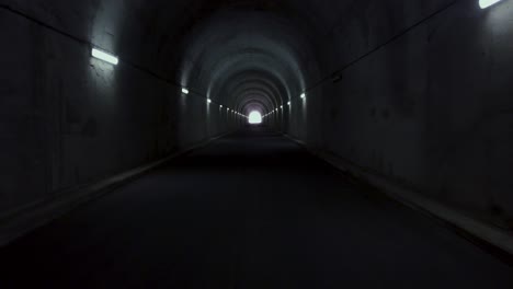 aerial flight through dark tunnel in the mountains with light on the horizon