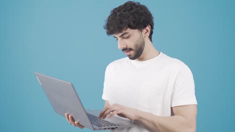 joven de pie usando una computadora portátil regocijándose, mirando la pantalla y sonriendo por la victoria.