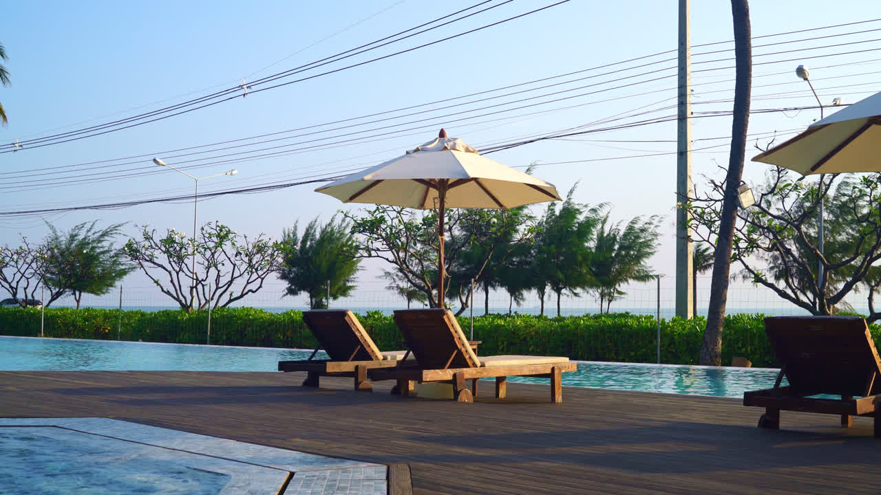 바다를 배경으로 수영장 주변에 침대 수영장이 있는 우산 - 휴일 및 휴가 개념