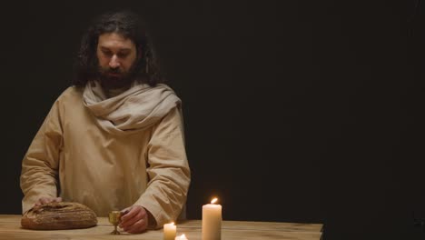 scatto in studio di un uomo che indossa abiti con capelli lunghi e barba che rappresenta la figura di gesù cristo che benedice il pane e il vino