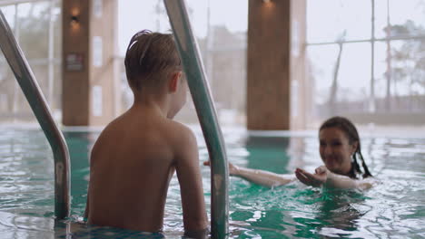 La-Madre-Le-Está-Enseñando-A-Su-Hijo-A-Nadar-En-La-Piscina.-Un-Niño-Alegre-Salta-Al-Agua-Para-Mamá,-Familia-Feliz.