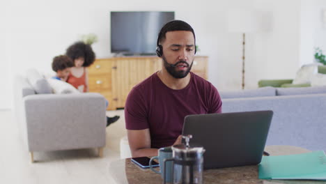 Mann-Mit-Headset-Telefoniert,-Während-Er-Zu-Hause-Einen-Laptop-Benutzt