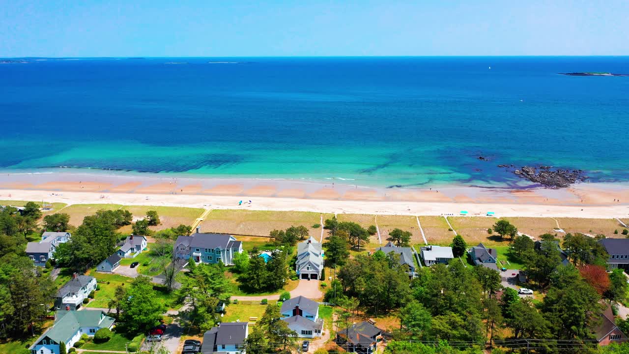 Flying drone captures Saco, Maine beaches alive with people. Crowds line the sand by the Atlantic Ocean, vacation homes in view, waves crash on shore. New England’s peak-season coastal beauty