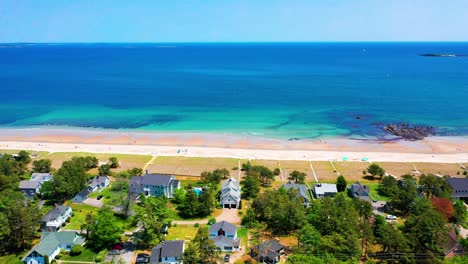 flying drone captures saco, maine beaches alive with people. crowds line the sand by the atlantic ocean, vacation homes in view, waves crash on shore. new england’s peak-season coastal beauty