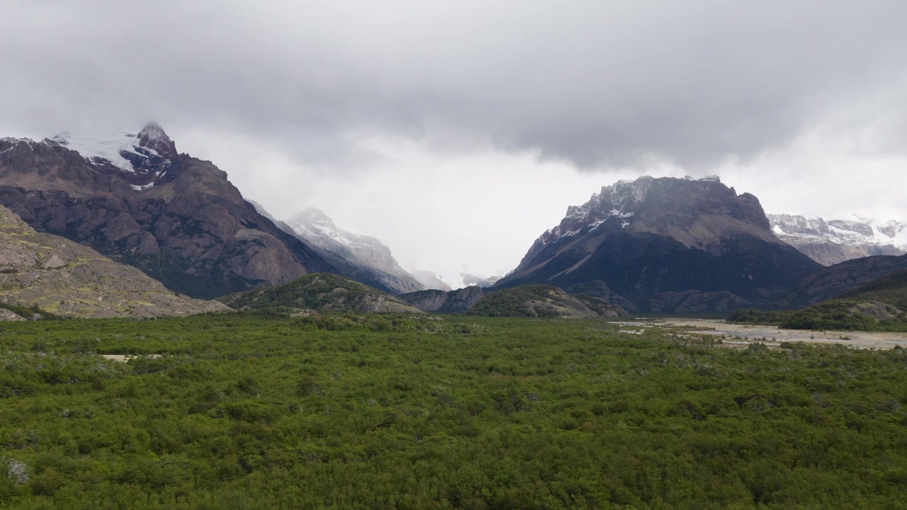 Le cime andine si ergono sopra una fitta boscaglia e valli glaciali vicino a El Chaltén, Santa Cruz, Argentina, sotto una drammatica copertura nuvolosa nella regione di Los Glaciares, ripresa con drone in lento sorvolo in avanti