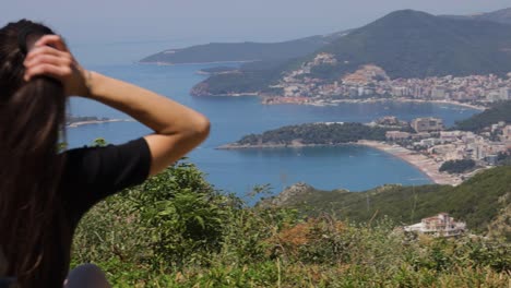 Girl-looking-at-seaside-town-from-hill,-plays-with-hair