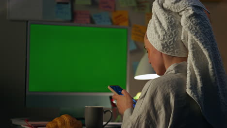 focused lady browsing smartphone night. girl sitting at green screen workplace