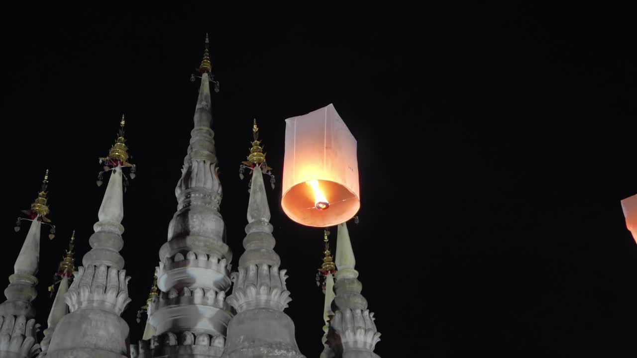 Farolillo de papel flotando en el cielo nocturno cerca de un templo tradicional tailandés durante las celebraciones del festival