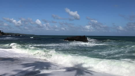 Rodando-Olas-Rompiendo-En-Una-Orilla-Arenosa-Con-Cocoteros