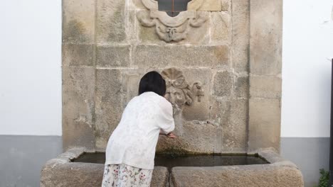 unrecognizable woman washes hands in ancient fountain of monsanto village