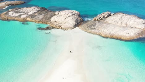 Excelente-Toma-Aérea-De-Un-Turista-Parado-Entre-Arena-Blanca-Y-Surf-Azul-Claro-En-Wylie-Bay,-Esperance,-Australia