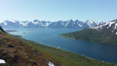 aerial view overlooking the arctic ocean, snowy lyngen mountains in the background, sunny, summer day, in rotsund, nordland, norway - descending, drone shot