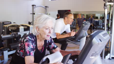 Aktives-älteres-Paar,-Das-Im-Fitnessstudio-Auf-Fahrradgeräten-Trainiert