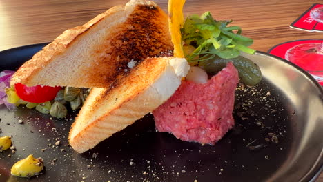 Tasty-beef-steak-tartare-with-toast-bread-and-a-pickle-on-a-plate,-raw-meat-dish,-4K-shot