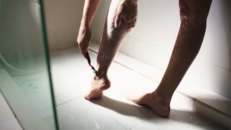 Close-up-shot-of-young-woman-shaving-her-legs-with-a-razor-while-taking-a-shower-in-the-morning