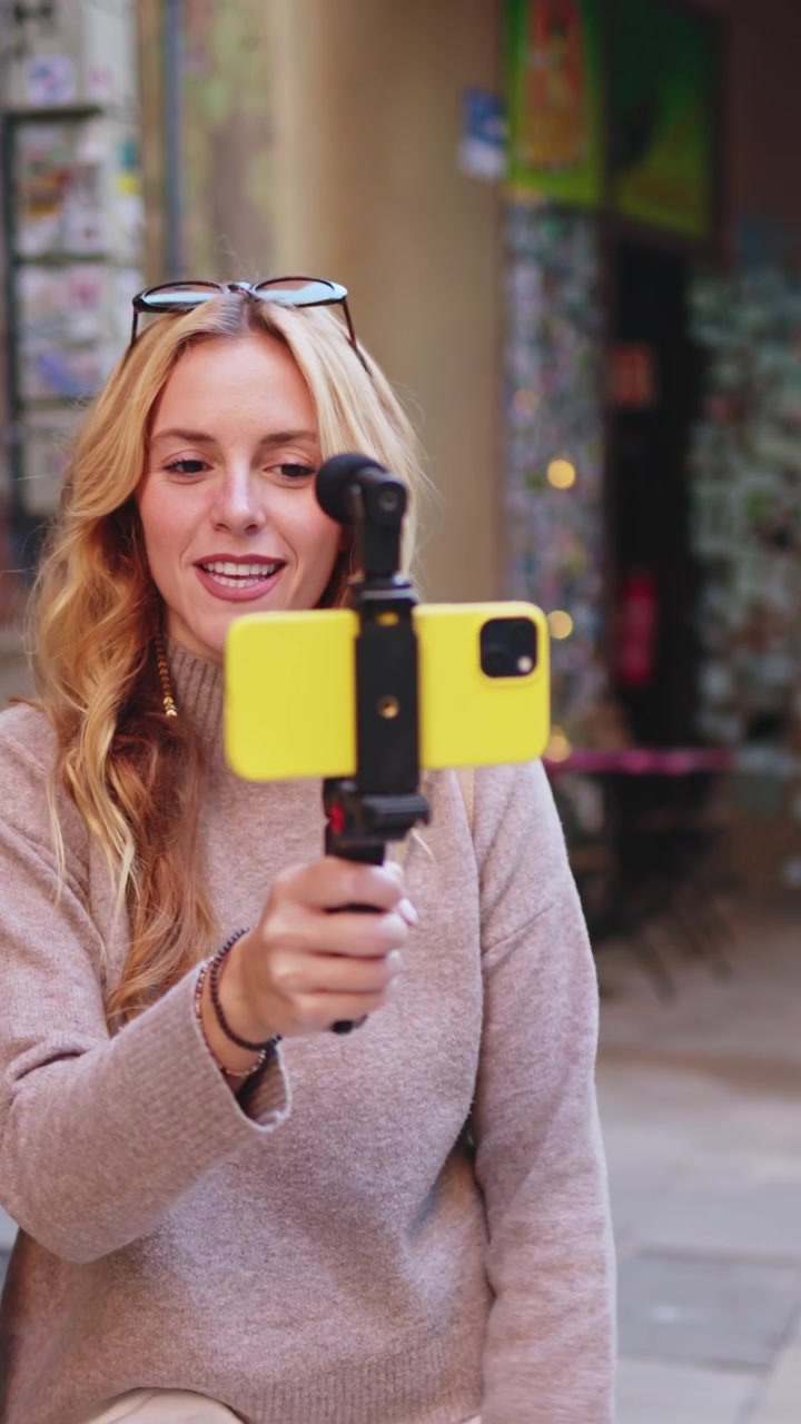 Giovane donna bionda che fa vlogging con lo smartphone per strada in città