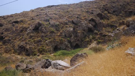 Handheld-Wide-Shot-of-a-Few-Dark-Mysterious-Caves-By-a-Mountain-Hill-Near-Red-Beach-in-Santorini-Greece