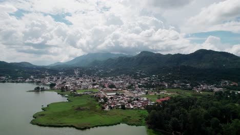 Drone zoom out from Cobán, Guatemala, showing lakeside town surrounded by lush vegetation and dramatic mountainous background