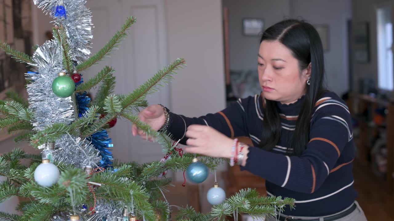 una mujer asiática baja los adornos de navidad del árbol al final de las vacaciones