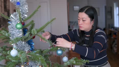 An-Asian-woman-takes-down-Christmas-ornaments-from-the-tree-at-the-end-of-the-holidays