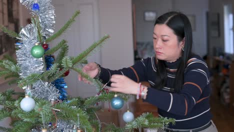 una mujer asiática baja los adornos de navidad del árbol al final de las vacaciones