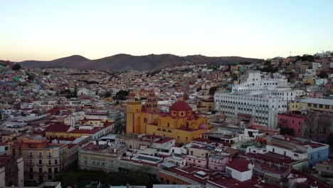 Aerial-panorama-view-of-the-buzzing-city-of-Guanajuato-in-central-Mexico,-with-magnificent-colonial-architecture-against-a-light-blue-sky