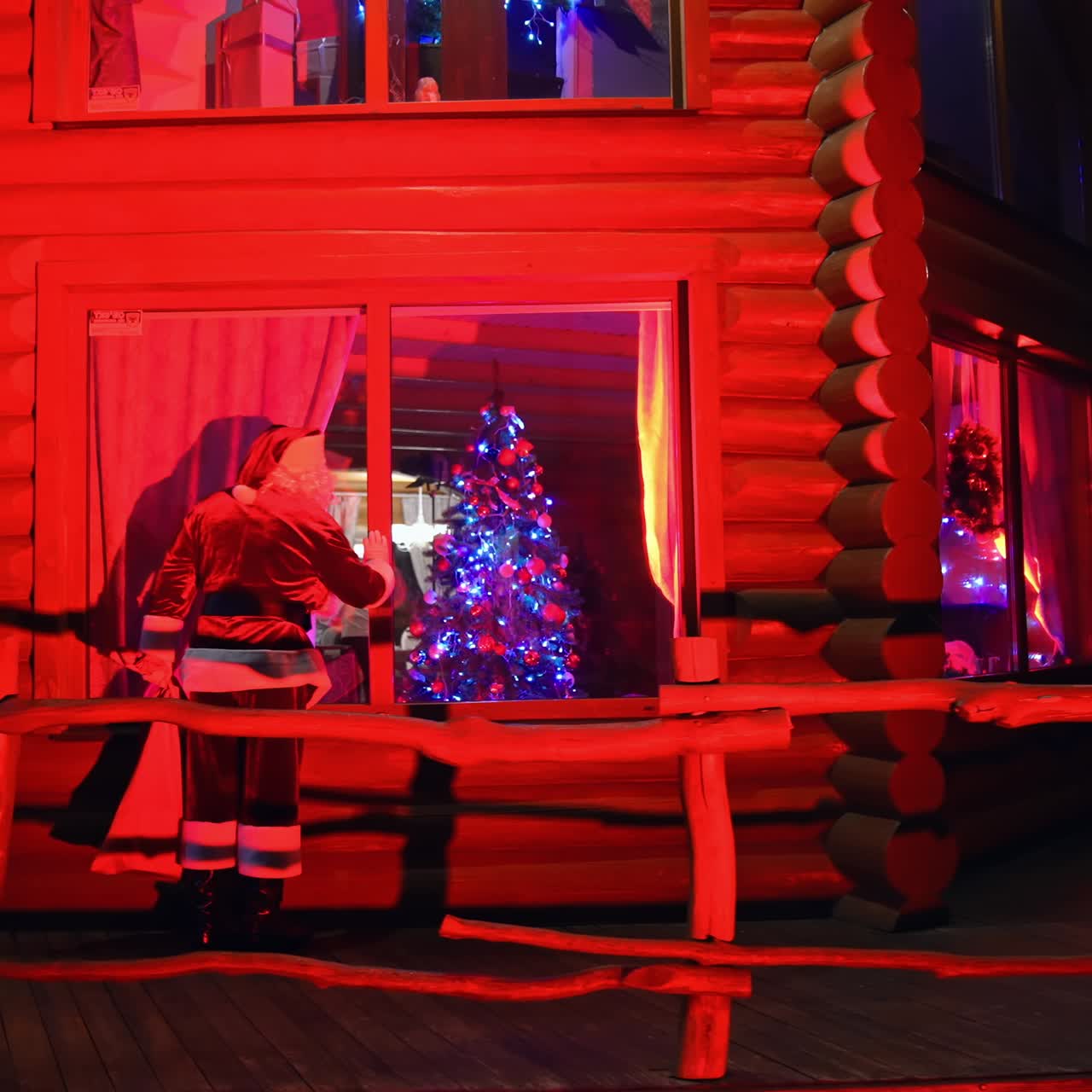 Santa Claus walking near the house. Father Frost at Christmas outdoors. Santa carrying presents at dark. Red lighting. Back view