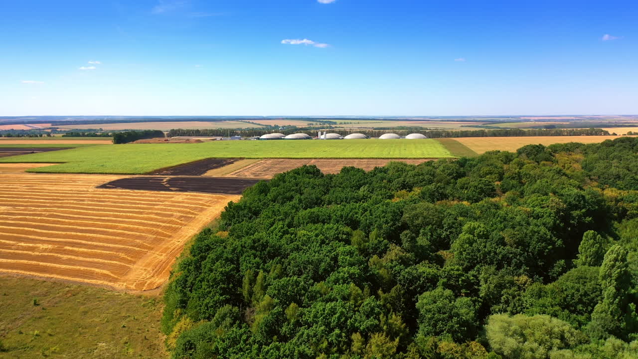 Drone flight over the green woods and fields to the tanks of biogas plant. Sustainable production of green energy.