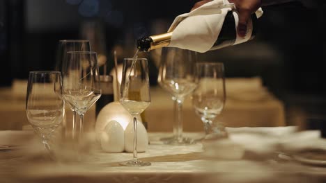 Hand,-Die-Teuren-Champagner-In-Ein-Sektglas-Auf-Dem-Tisch-Gießt---Selektiver-Fokus