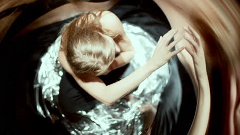 woman sitting on silver floor, touching at wavy distorted reflections