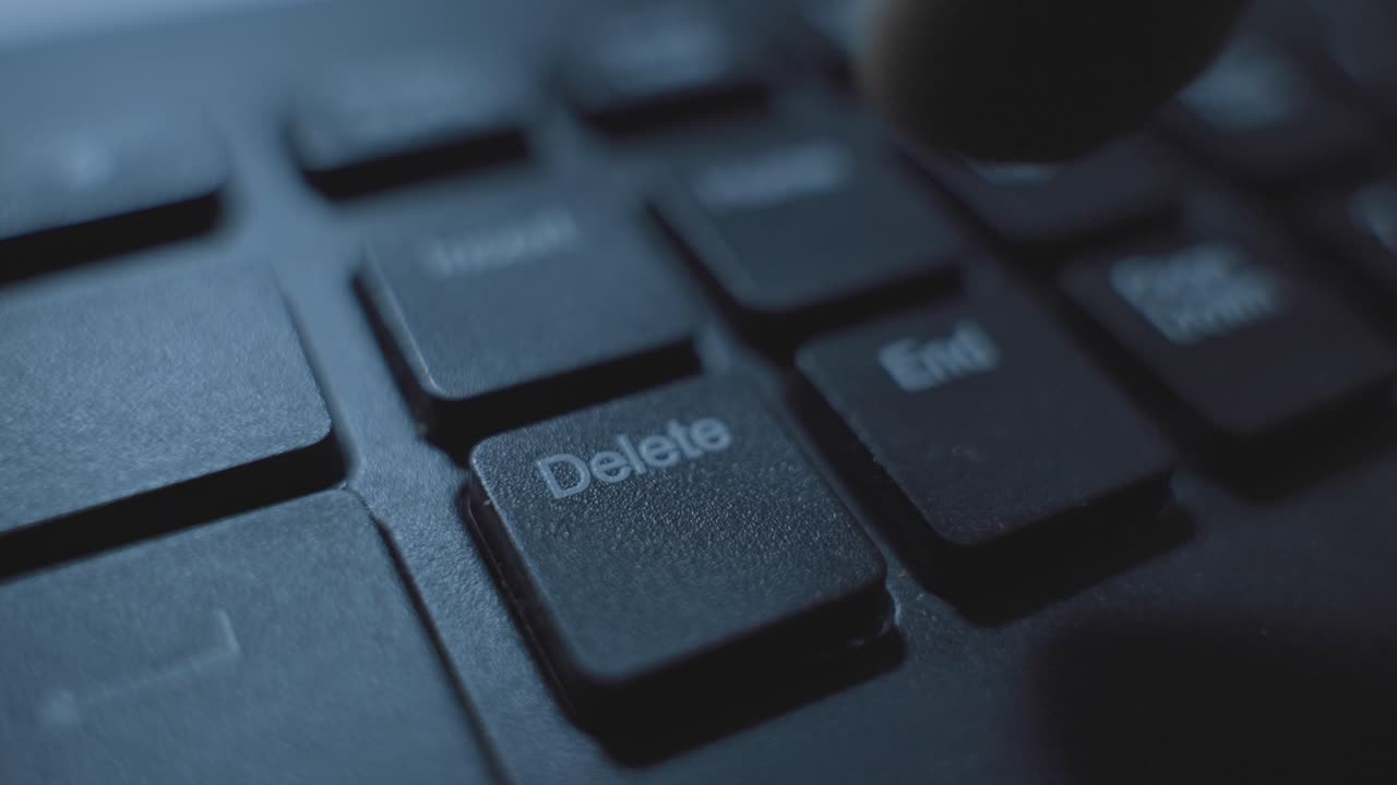 Close up on finger pressing Delete key on computer keyboard in dark office desk. Mysterious dark web suspicious activity. Erasing data and information or removing text and files. Click on keypad of PC