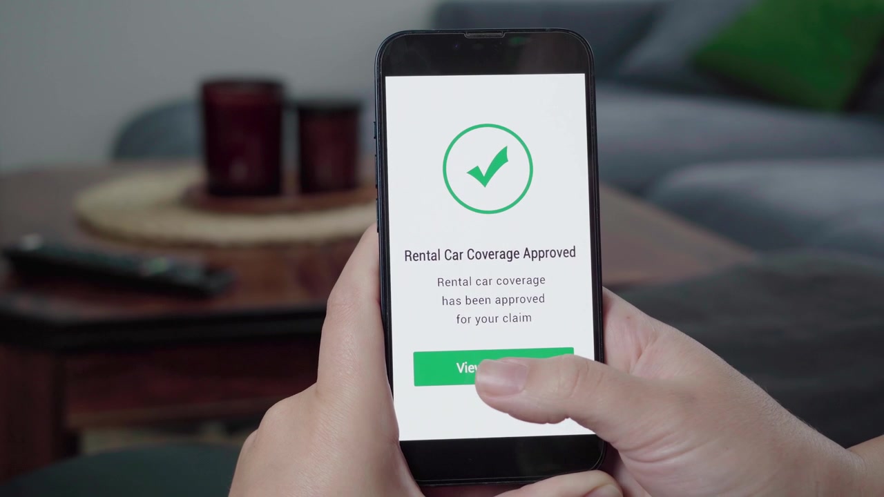 Una persona controlla un'app per le richieste di risarcimento mentre appare un messaggio "Copertura Auto a Noleggio Approvata" con una spunta verde e il pulsante "Visualizza prenotazione".