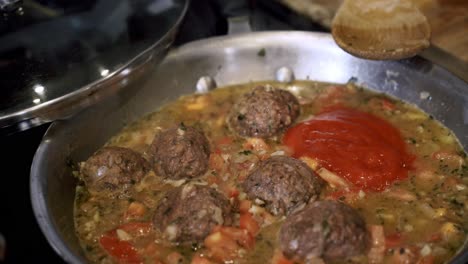 adding organic tomato sauce into pan of meatballs preparing ingredients to make vegan beyond meatballs with spaghetti and meat sauce