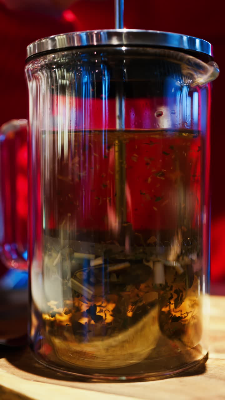 Close up of a woman pressing down the tea leaves with the help of a French press. Vertical