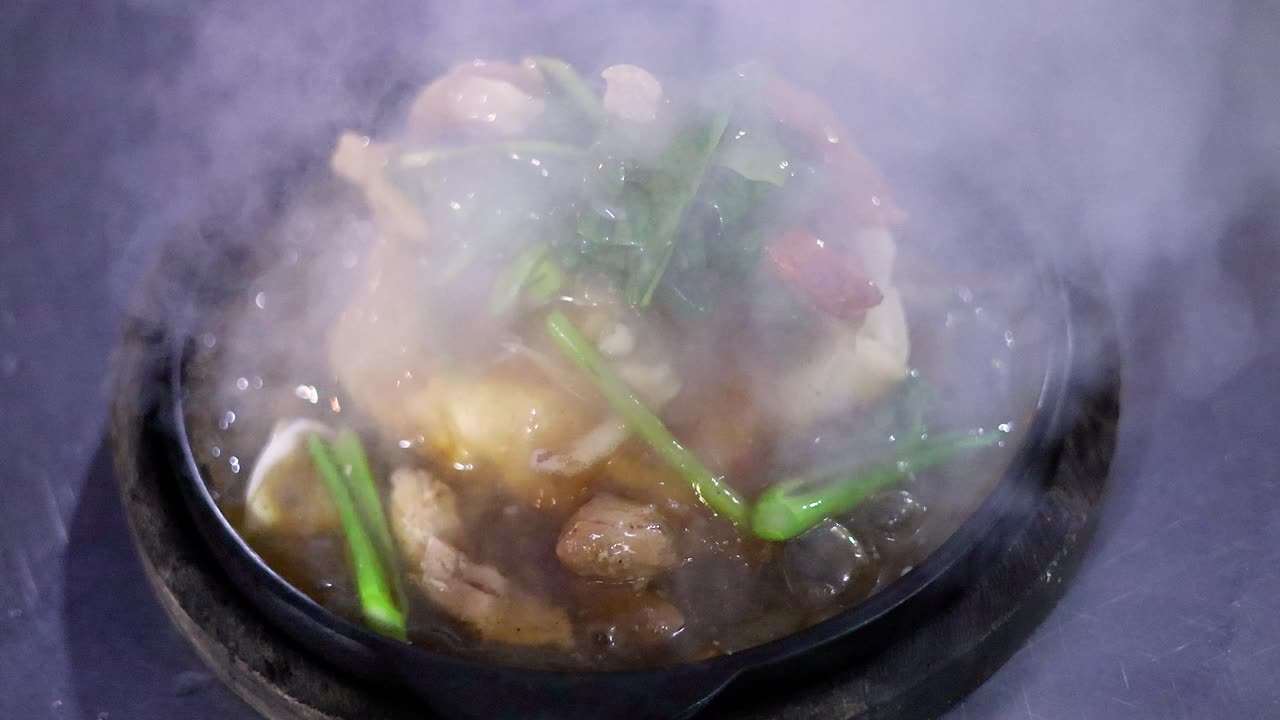 Sizzling fried noodles with vegetables on a hot plate, steam rising under dramatic night lighting