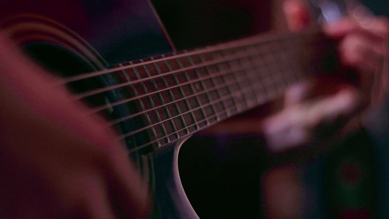 Warm-toned close-up of an acoustic guitar being strummed, with shallow depth of field highlighting strings and fretboard. Rhythmic hand movement creates an intimate, cinematic musical moment. Close-up