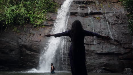 silhouette view of a women outstretching her arms in front of waterfall at odisha, india