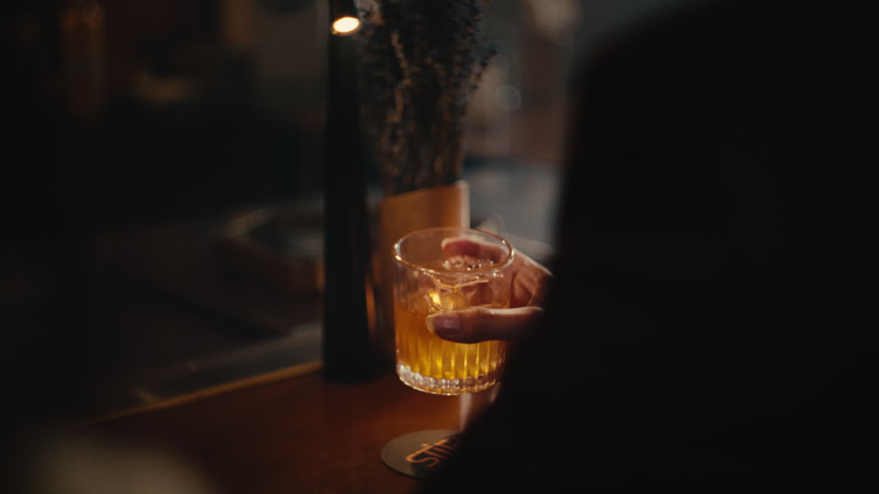 Hand holding a whiskey cocktail at a bar at night