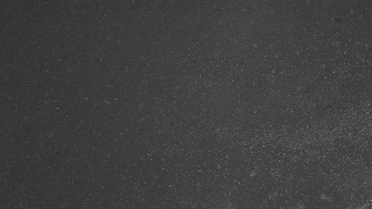 fuertes gotas de lluvia cayendo sobre una carretera asfaltada filmadas desde arriba