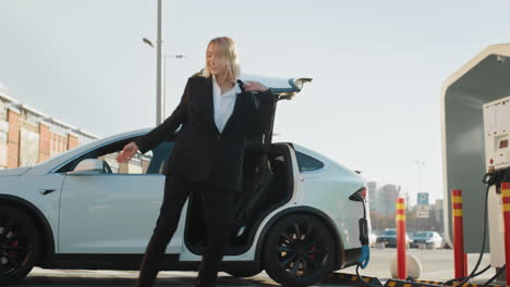 happy woman dancing by electric car at charging station
