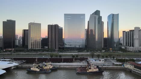 dolly aéreo de barcos en los muelles de puerto madero con edificios de gran altura en el fondo al atardecer, buenos aires.